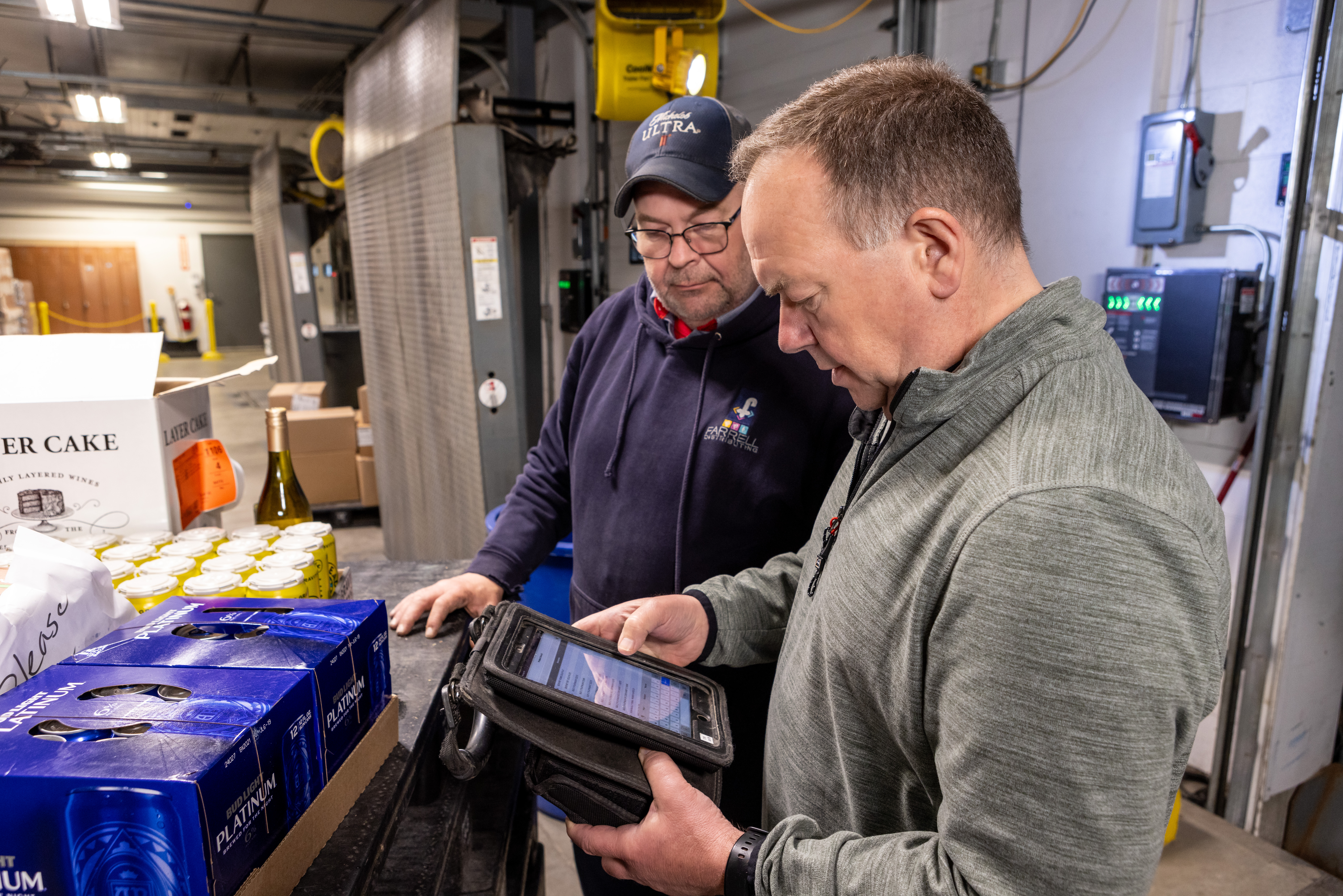 Warehouse worker using a handheld tablet to check inventory beside shrink-wrapped pallets of canned beverages